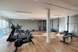 Ein Fitnessstudio mit Cardiogeräten, Krafttrainingsstationen und einer Sitzbank.