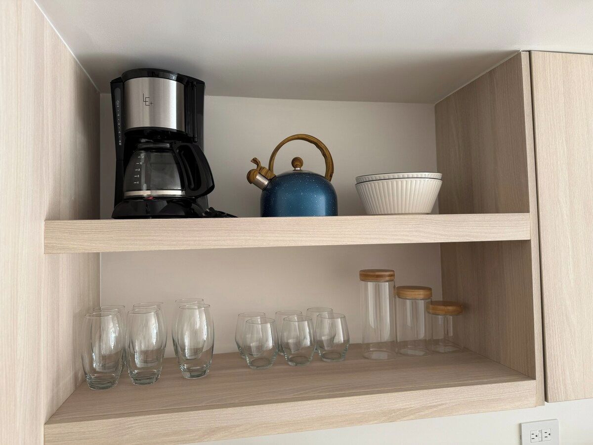 Uma prateleira na cozinha com cafeteira, chaleira azul e vários copos e potes de vidro.