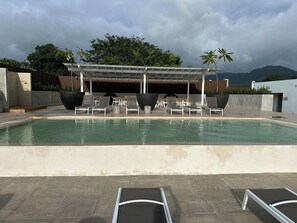 Ein Schwimmbecken mit Liegestühlen und einer überdachten Sitzgelegenheit.
