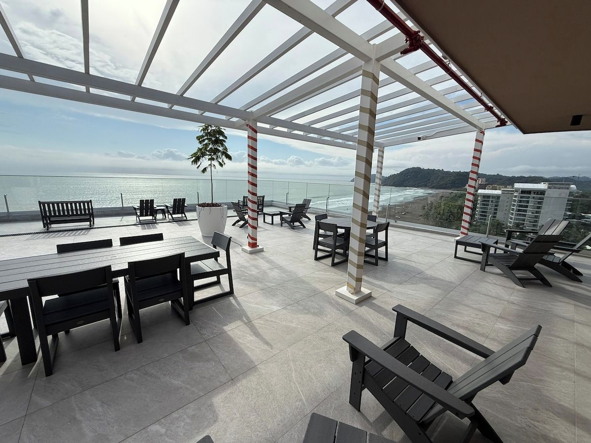 Une terrasse sur le toit avec des sièges extérieurs, un palmier et une vue sur l’océan.