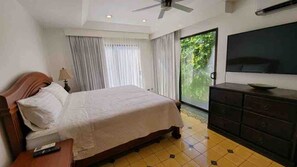 Habitació d'hotel amb un llit, televisió, aparador i finestra amb cortines.