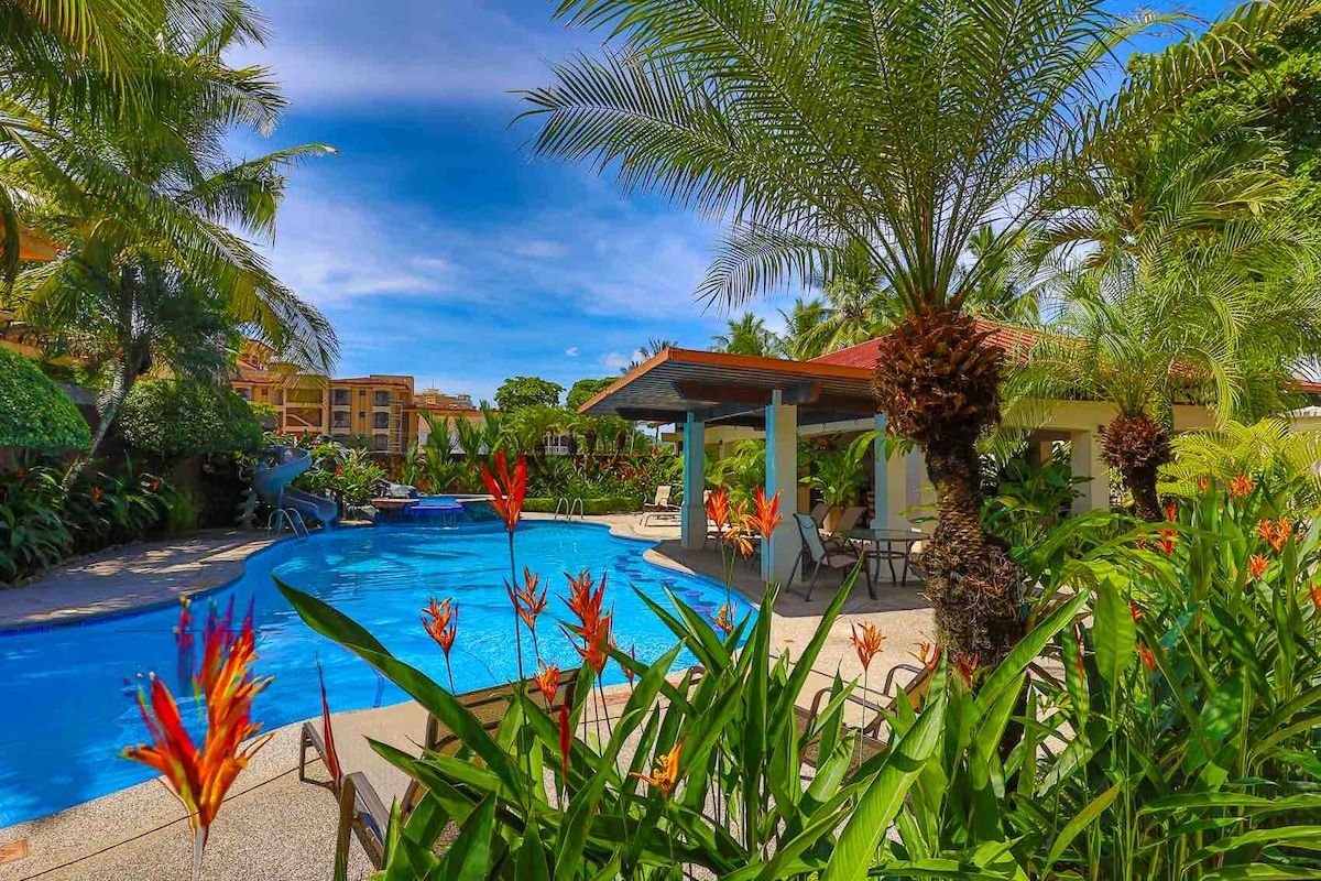 A swimming pool surrounded by lush greenery and a covered seating area.