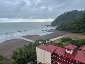 Eine Küstenansicht mit Strand, bewaldetem Hügel und einem Gebäude mit roten Dächern.