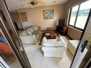 Ein Wohnzimmer mit einer Couch, einem Couchtisch und einem Fernseher. An den Wänden hängen zwei Gemälde.