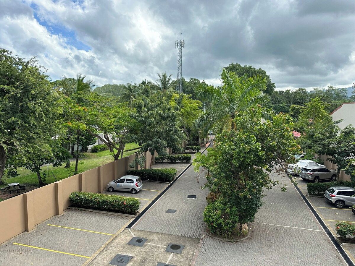 A parking area with multiple cars, surrounded by greenery and a tall communication tower.