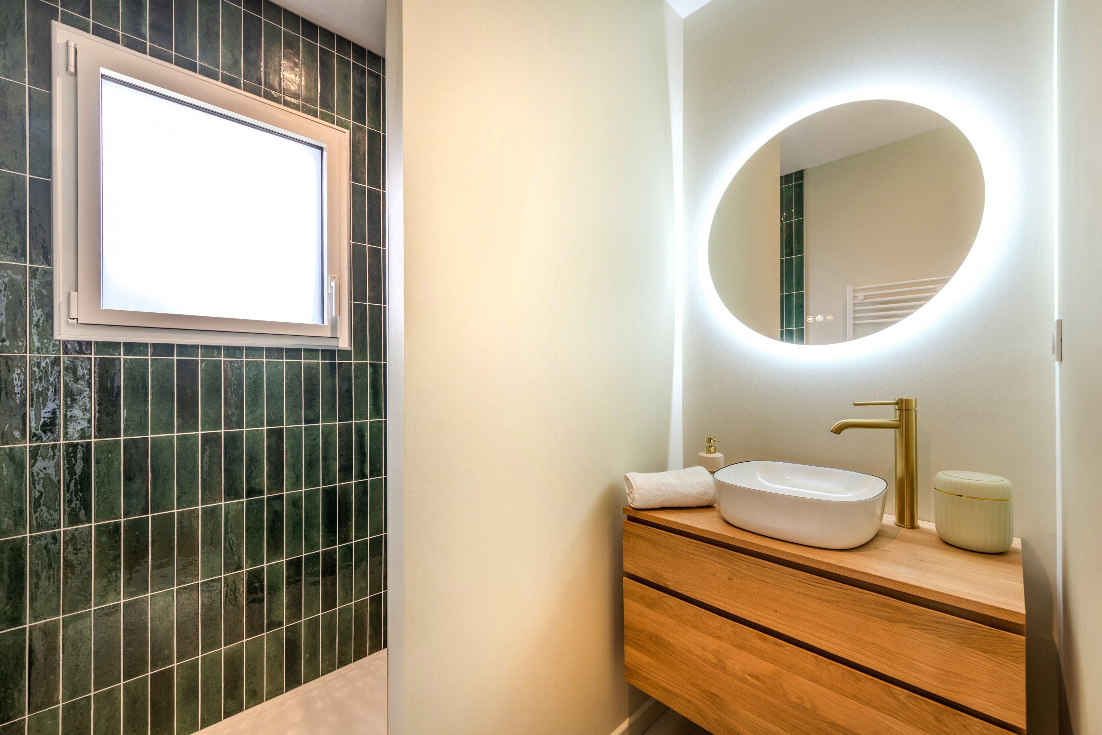 A bathroom with a white sink, a round mirror with a light, and a wooden vanity.