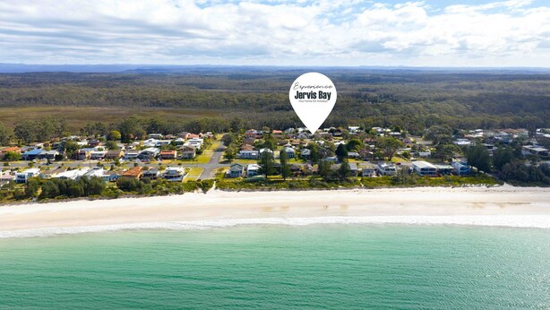 Vue aérienne d’une zone résidentielle côtière, avec des maisons, une plage et un paysage boisé.