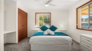 Une chambre à coucher comprenant un lit, une armoire, une table de chevet, une lampe, une fenêtre et un ventilateur de plafond.