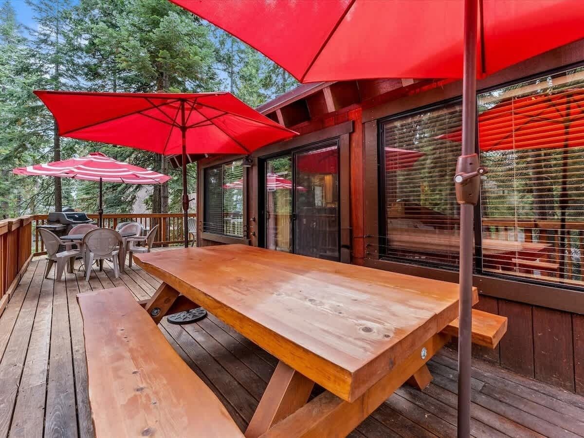 Une terrasse en bois avec une grande table de pique-nique et des parasols rouges.