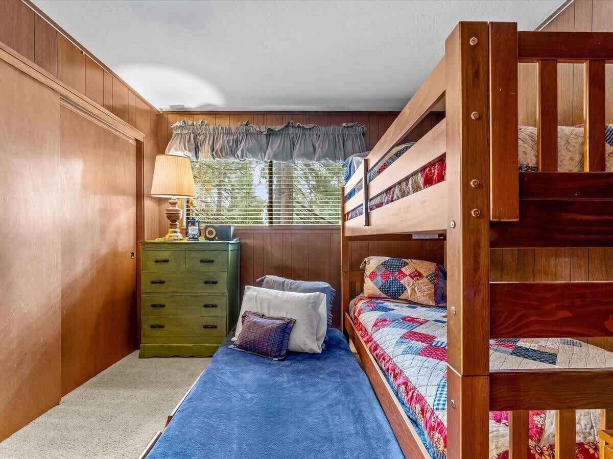 Habitación con literas, un aparador de madera, una lámpara y una ventana con cortinas.