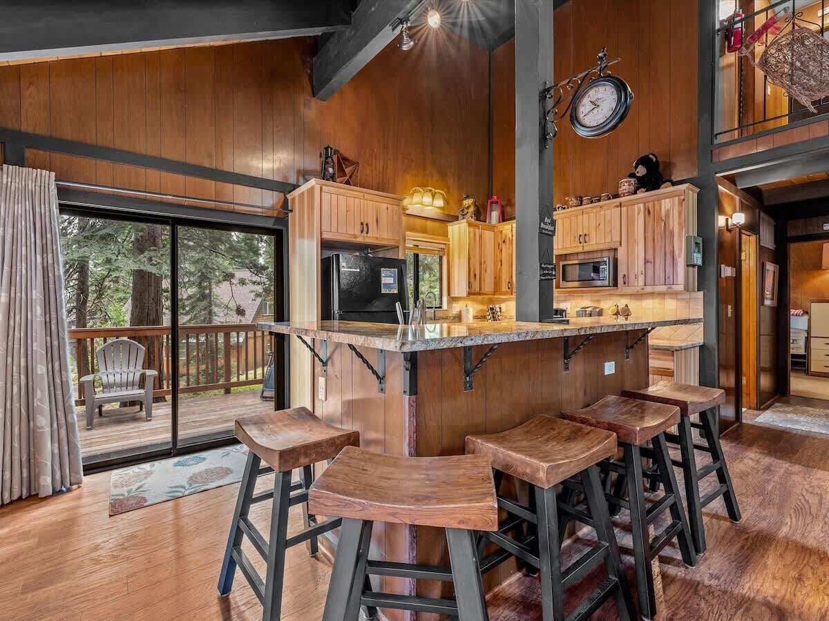 A kitchen with wooden cabinets, a bar area with stools, and a large window overlooking a deck.