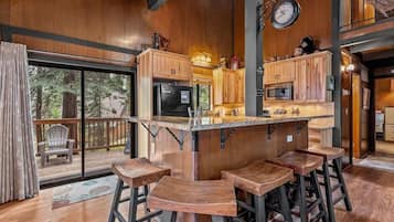 A kitchen with wooden cabinets, a bar area with stools, and a large window overlooking a deck.