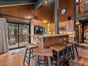 Eine Küche mit Holzausstattung, einer Bar inklusive Sitzhocker und einem großen Fenster mit Blick auf eine Terrasse.