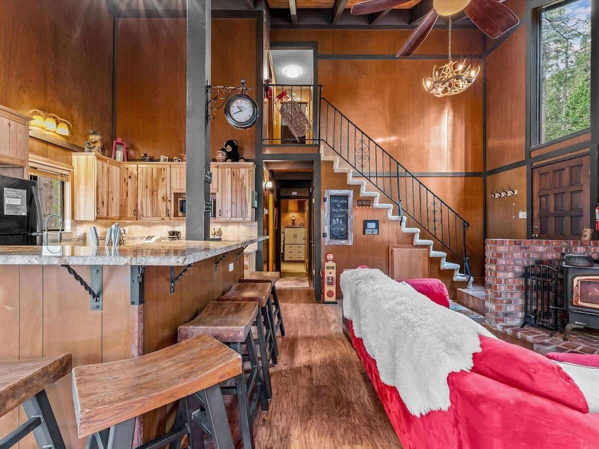 Un interior rústico con barra de madera, una escalera, chimenea y una zona de estar acogedora.