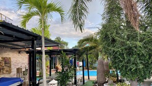A covered outdoor area with a pool, palm trees, and potted plants. - Villa Na Wande Sattahip (Sattahip)
