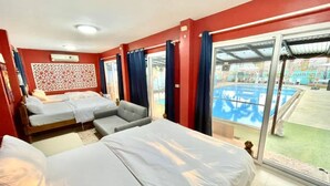 A hotel room with two beds, a sofa, a decorative wall panel, and a large window overlooking a swimming pool. - Villa Na Wande Sattahip (Sattahip)