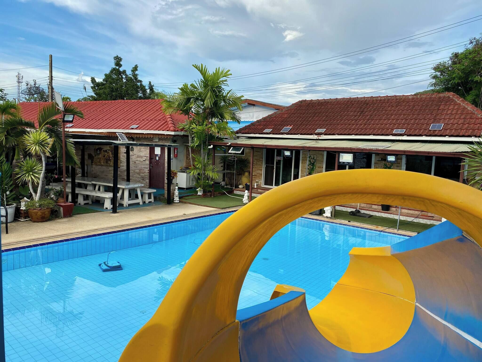 A swimming pool with a slide, surrounded by buildings with red roofs and outdoor seating areas.