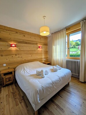 A bedroom with a wooden headboard, a large bed with white linens, two bedside lamps, and a window with curtains.