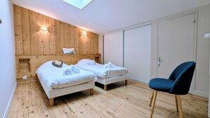 Quarto com duas camas, painéis de madeira nas paredes, um guarda-roupa e uma cadeira azul.