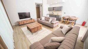 A modern living room with a sofa, coffee table, TV, and a small kitchen area with a dining set. - Altındere Vadi Hotel (Akyazi)