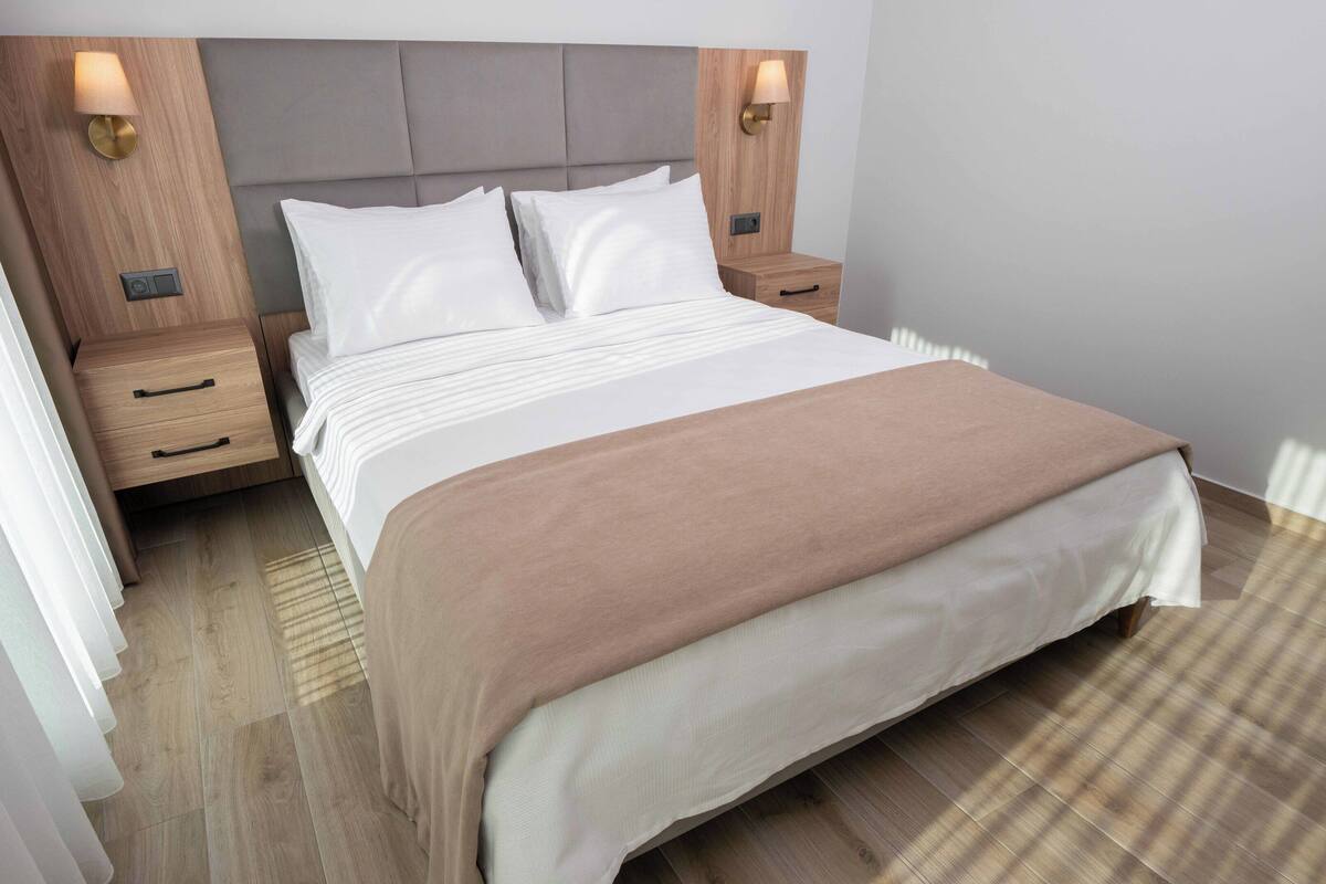 A neatly made bed with a headboard, two bedside tables with lamps, and a wooden floor.
