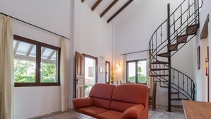 A living room with a sofa, a wooden coffee table, a spiral staircase, and large windows. - Family-friendly Stay With Pool Access (Pozo Alcon)