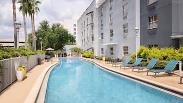 A swimming pool with lounge chairs and a building with multiple windows.
