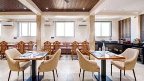 A modern dining area with wooden tables and chairs, a ceiling fan, and large windows. - Palette Hotel Pune, Midc Chinchwad (Pune)