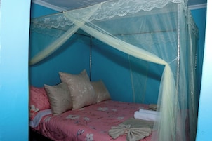 Una cama individual con una colcha floral rosa, almohadas color beige y un dosel blanco.