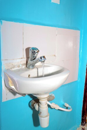 Un évier blanc avec de l’eau qui coule, fixé sur un mur bleu recouvert de carreaux blancs.
