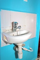 Un lavamanos blanco con agua corriente, instalado en una pared azul con azulejos blancos.