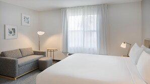 A hotel room with a large bed, a grey sofa, a small table, a floor lamp, and two framed pictures on the wall. - Fully Equipped Kitchen in Modern Suite with Airport Shuttle and Swimming Pool (Tampa)