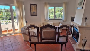 A living room with a sofa, a wooden chair, a fireplace, and a view of the outdoors. - Charming apartment near the beach! Condominium with pool and playground (Amoreira)