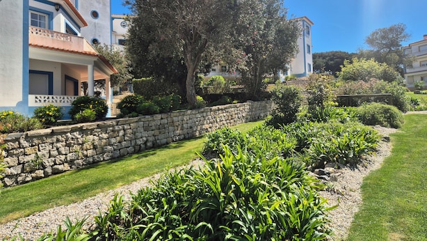 A building with a stone wall, a large tree, and well-maintained greenery. - Charming apartment near the beach! Condominium with pool and playground (Amoreira)