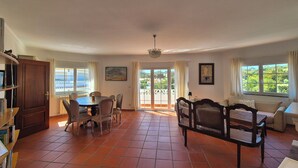 A spacious living area with a dining table, chairs, a sofa, and a view through a glass door to the outdoors. - Charming apartment near the beach! Condominium with pool and playground (Amoreira)