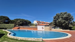 A swimming pool with a stone border, a brick patio, and a building with red-tiled roofs in the background. - Charming apartment near the beach! Condominium with pool and playground (Amoreira)