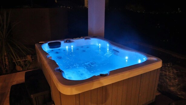 A wooden hot tub with a blue light, surrounded by plants.