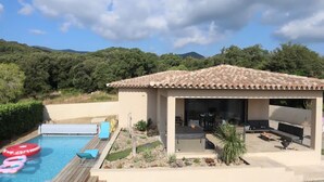 A pool with lounge chairs, a covered patio with seating, and a view of the surrounding hills.