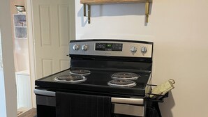 Una cocina con estufa de acero inoxidable, puerta de horno negra y estante de madera sobre la estufa.