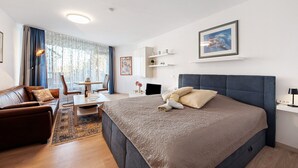 Una habitación de hotel moderna con una cama grande, un sofá, un escritorio con silla, una mesita y un ventanal con cortinas.