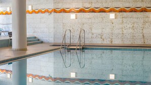 Una piscina interior con paredes de azulejos, escalones de acceso y barandillas de metal.