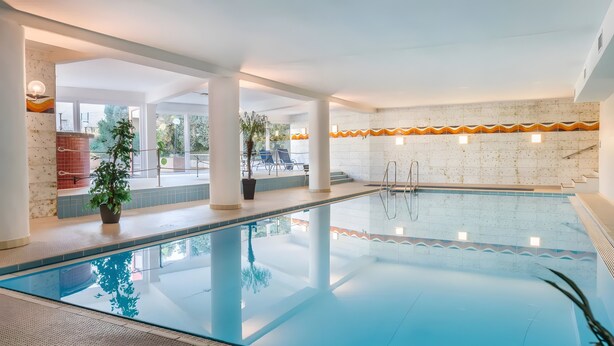 Una piscina interior con agua cristalina, rodeada por un muro con azulejos y un ribete naranja decorativo, y plantas en macetas.