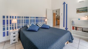 A bedroom with a bed, bedside tables, a bookshelf, and a door leading to a bathroom. - Gîte 'Romarin' with Mountain View, Wi-Fi and Air Conditioning (Entrechaux)