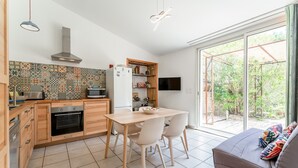 A modern kitchen with wooden cabinets, a built-in oven, and a dining area with chairs. - Gîte 'Romarin' with Mountain View, Wi-Fi and Air Conditioning (Entrechaux)
