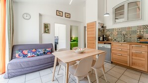 A modern kitchen with a wooden cabinet, a dining table with chairs, and a sofa with a colorful cushion. - Gîte 'Romarin' with Mountain View, Wi-Fi and Air Conditioning (Entrechaux)