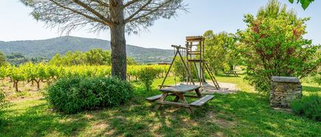 A picnic area with a wooden table and benches, surrounded by greenery and a stone wall.