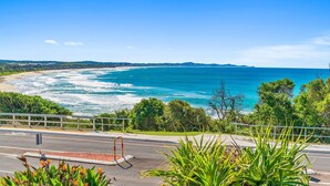 A coastal road with a guardrail, leading to a beach with waves crashing onto the shore.