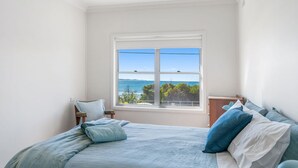 A bedroom with a bed, pillows, a nightstand, and a window with a view of the sea.