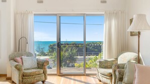 A room with two floral-patterned armchairs, a floor lamp, and a view of the sea through a sliding glass door.