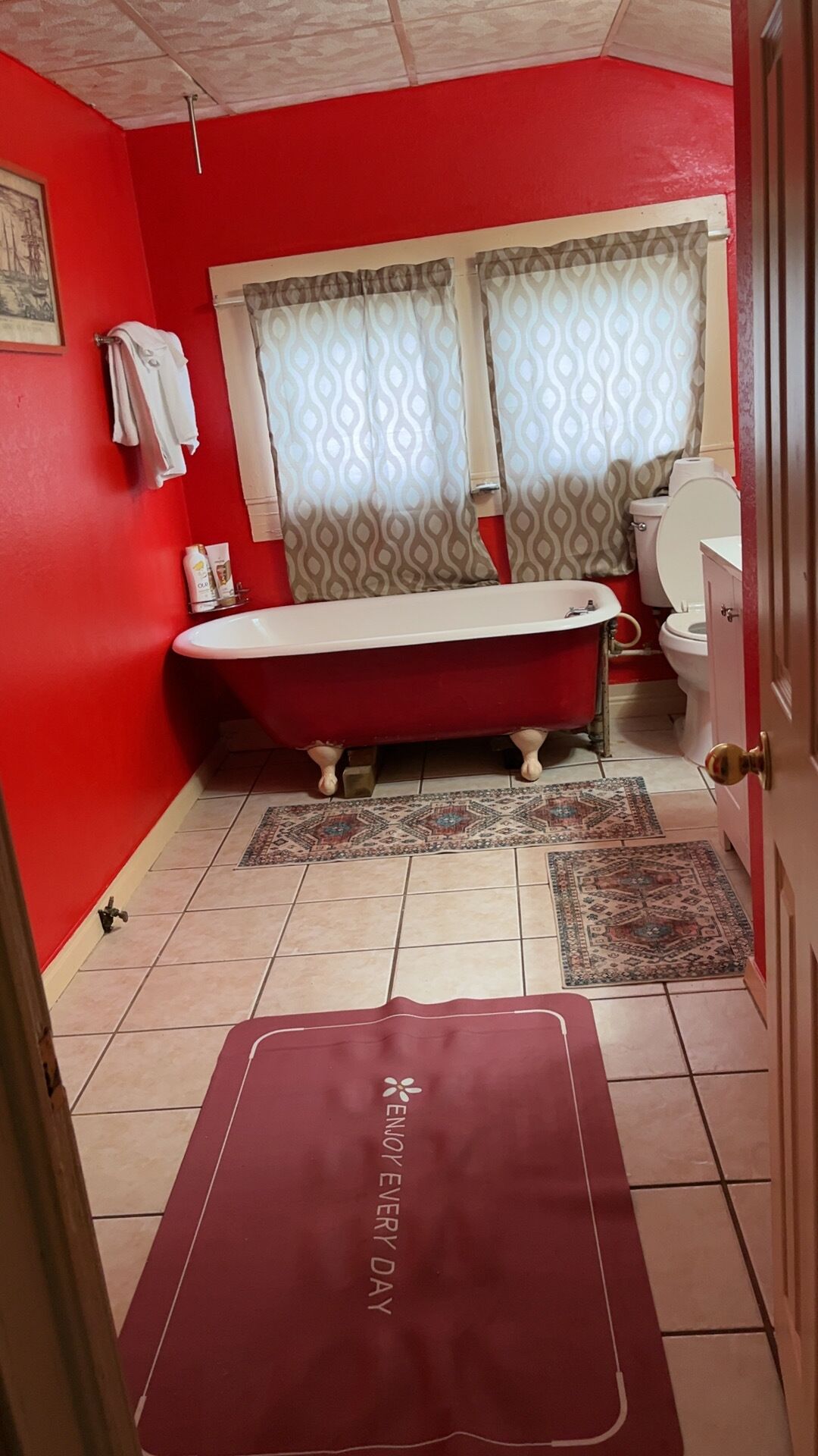 Un bagno con una vasca da bagno rossa, un water e un lavandino. Si nota una tenda decorata e un tappeto sul pavimento.